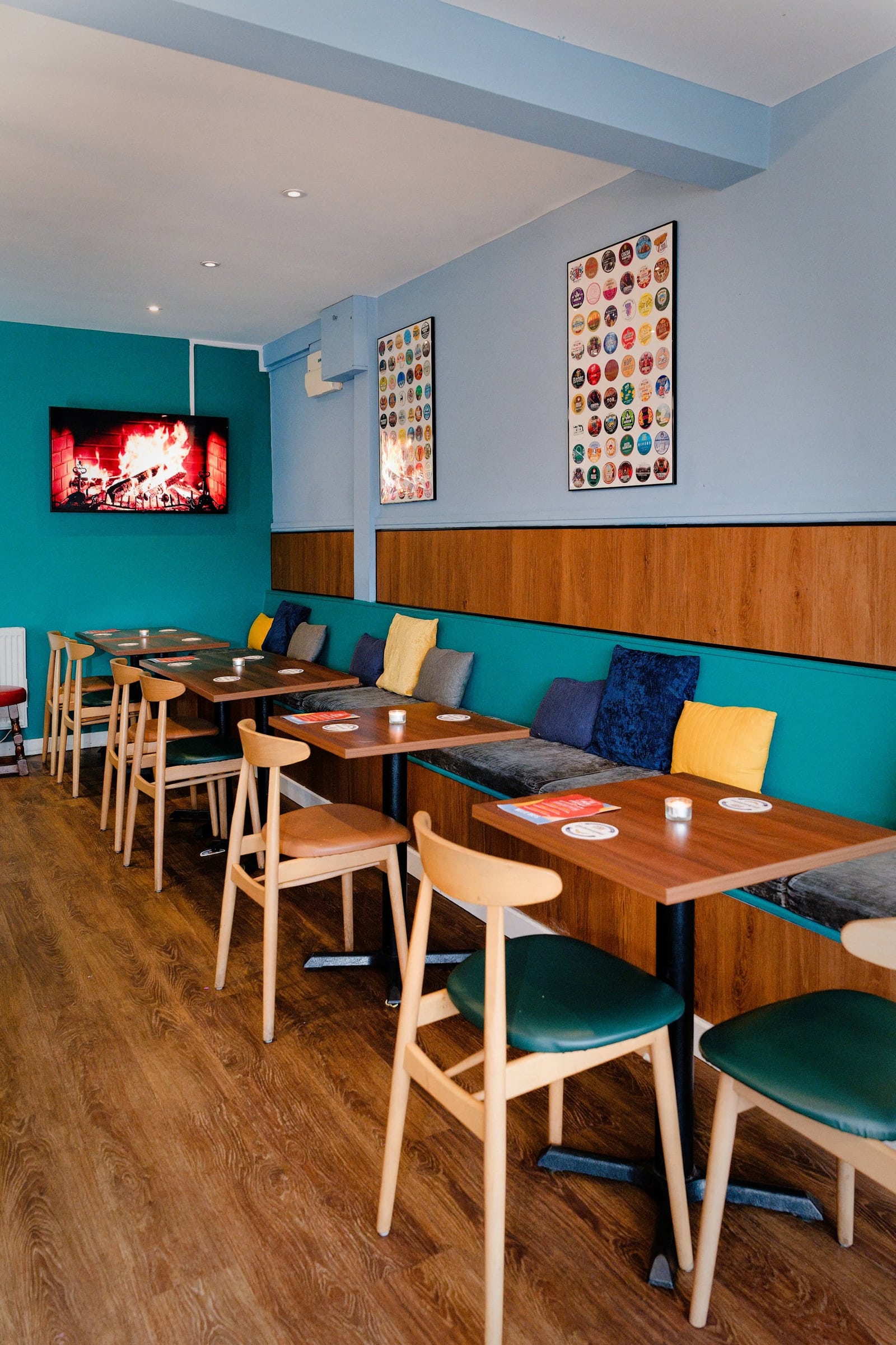 A cosy corner of Woodside with teal bench seating, wooden tables and framed beer labels
